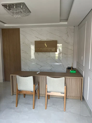Recepção do consultório com bancada de madeira clara, cadeiras estofadas e letreiro dourado com o nome da clínica